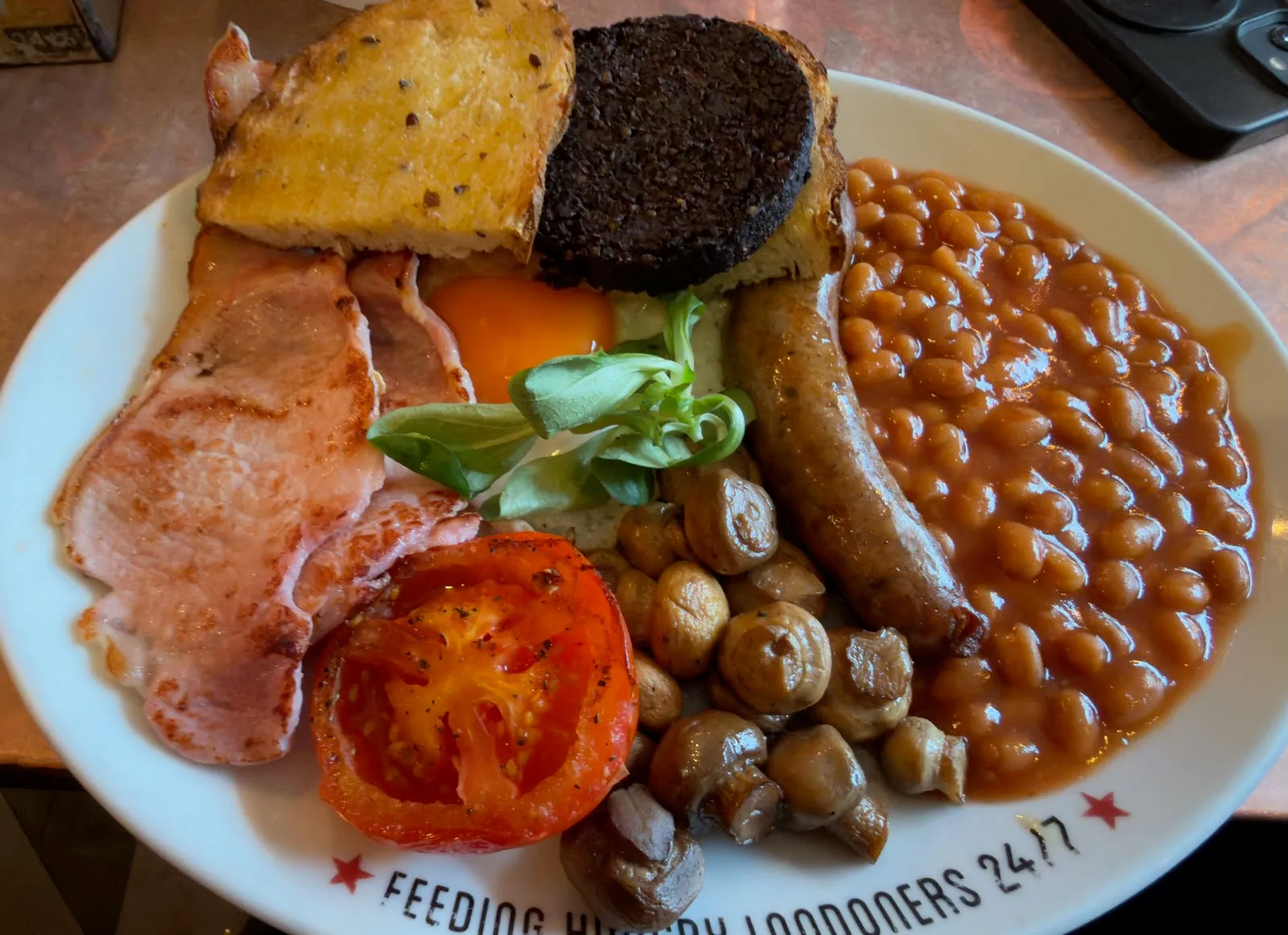 A full English breakfast on a plate reading "Feeding Hungry Londoners 24/7" at Polo Bar