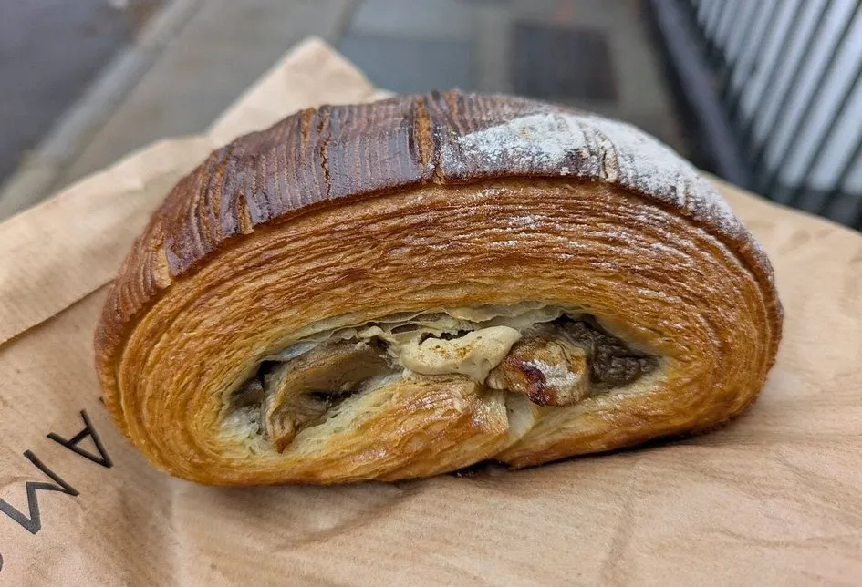 A thick laminated pastry roll on a brown paper bag, cut open to show its many layers wrapped around a mushroom filling
