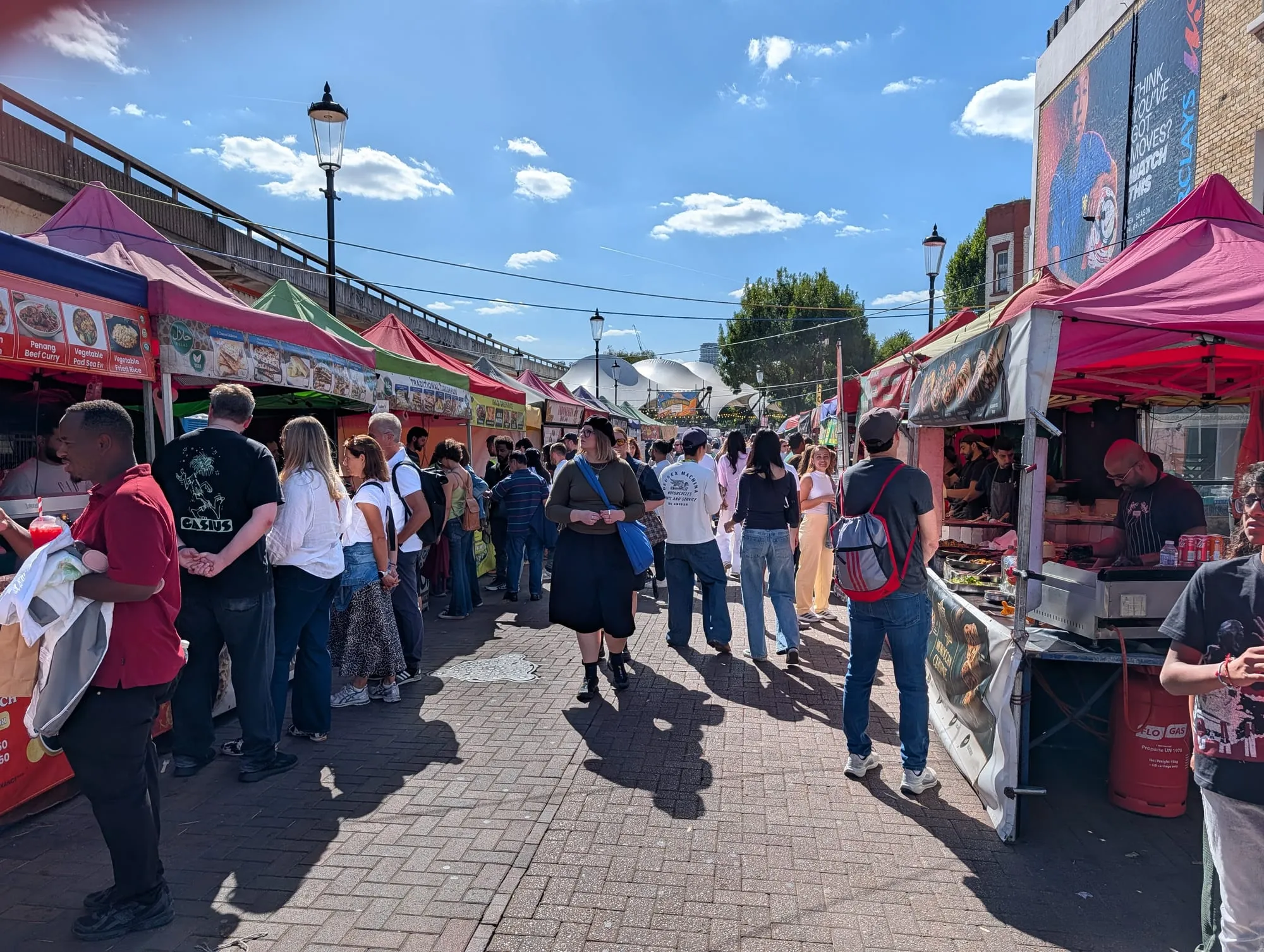 Market stalls with brightly coloured canopies running under the Westway flyover on Acklam Road, busy with shoppers
