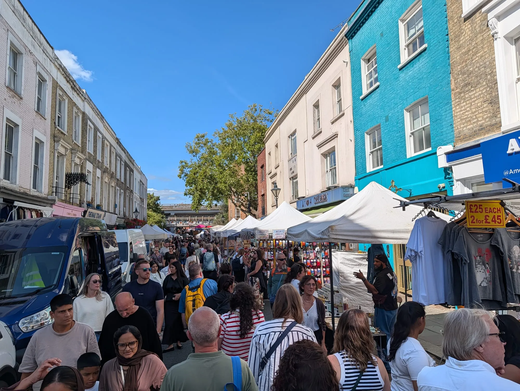 A dense crowd filling Portobello Road between market stalls and pastel shopfronts