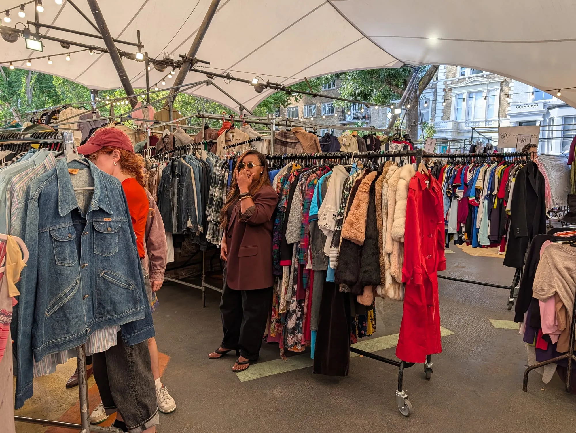 Rails of second-hand coats, dresses and denim jackets under a white canopy at the vintage market beneath the Westway