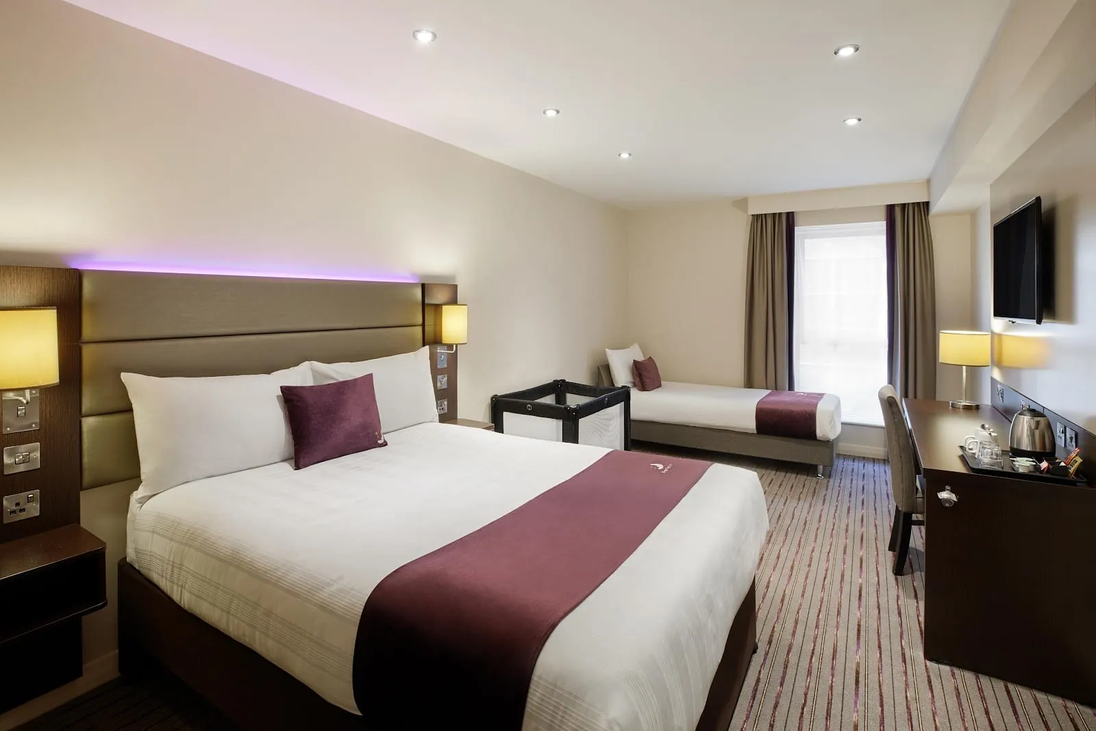 A twin room at Premier Inn London County Hall, with a double bed, a single bed and a travel cot set up between them