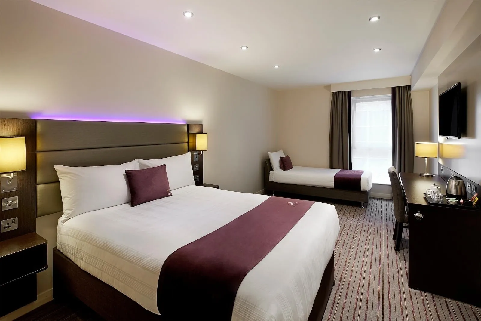 A room at Premier Inn London Docklands (ExCeL) with a double bed, a single bed by the window and a desk