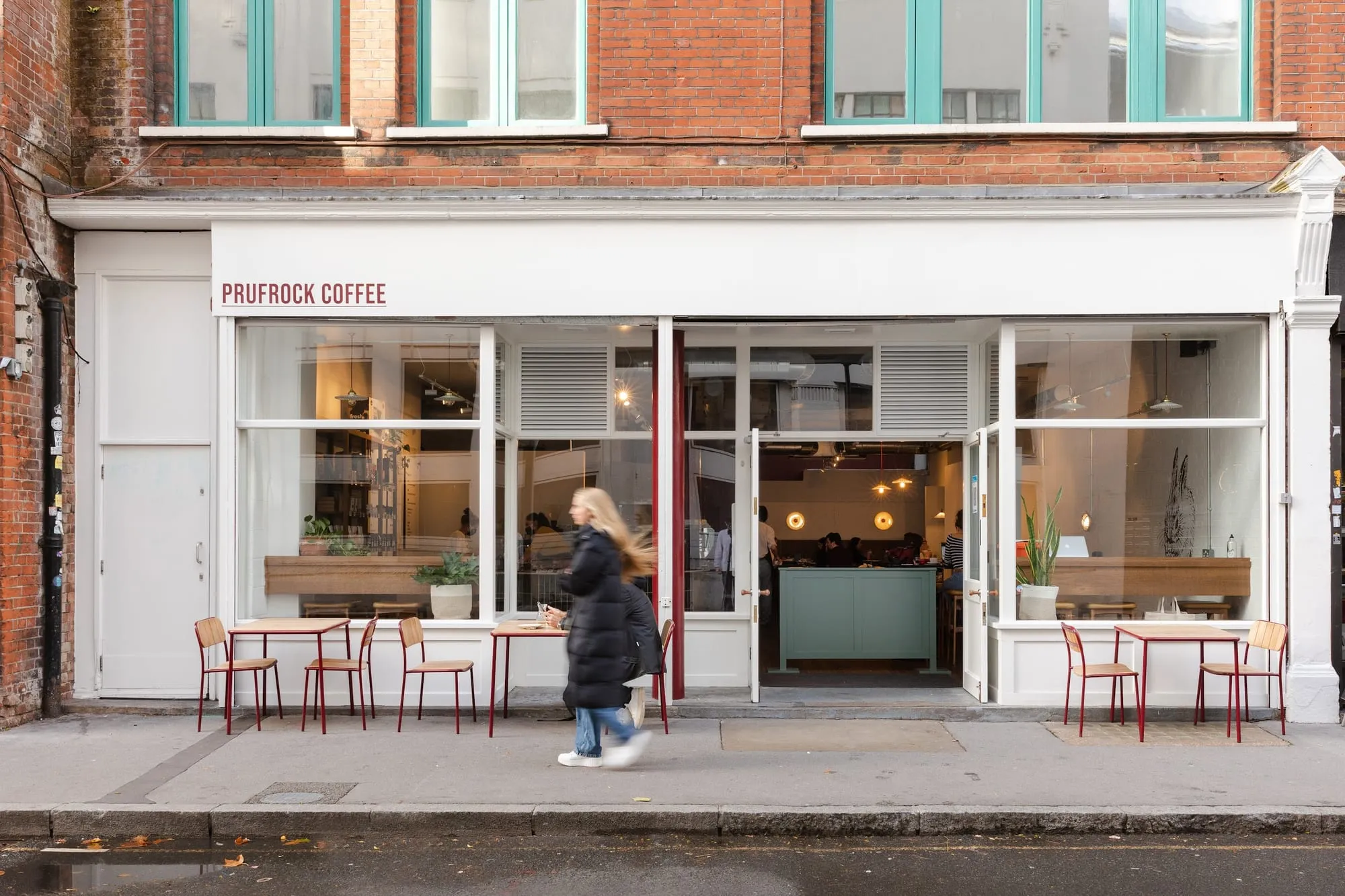 The Leather Lane frontage of Prufrock Coffee, with red pavement tables outside and the counter visible through the window