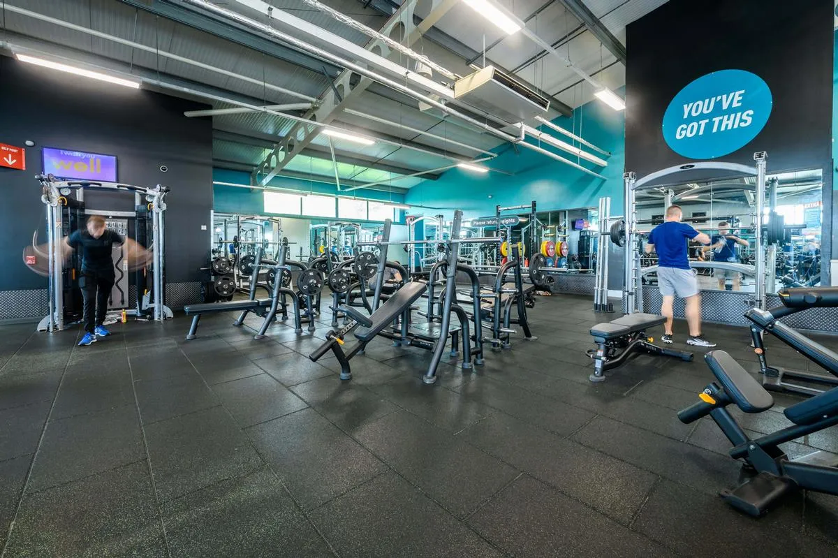 A PureGym free-weights floor - Olympic benches and loaded barbells on rubber matting, a teal wall behind reading YOU'VE GOT THIS