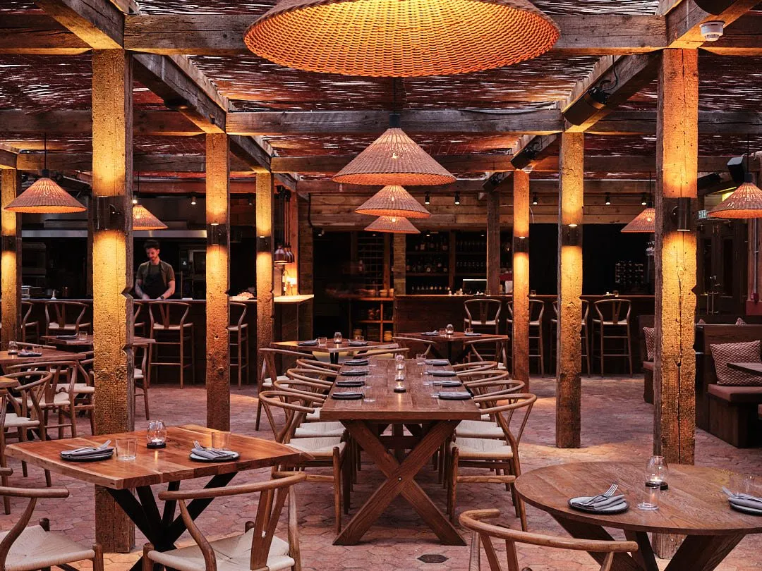 Pyro's dining room, with wooden posts and beams, woven pendant lamps, wishbone chairs and long wooden tables on a terracotta floor
