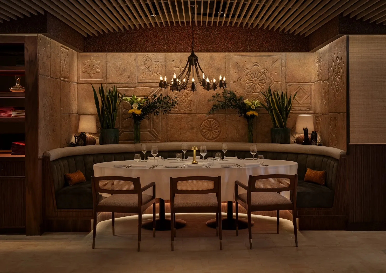 The dining room at Quilon with carved sandstone relief tiles, a central chandelier and a curved banquette table