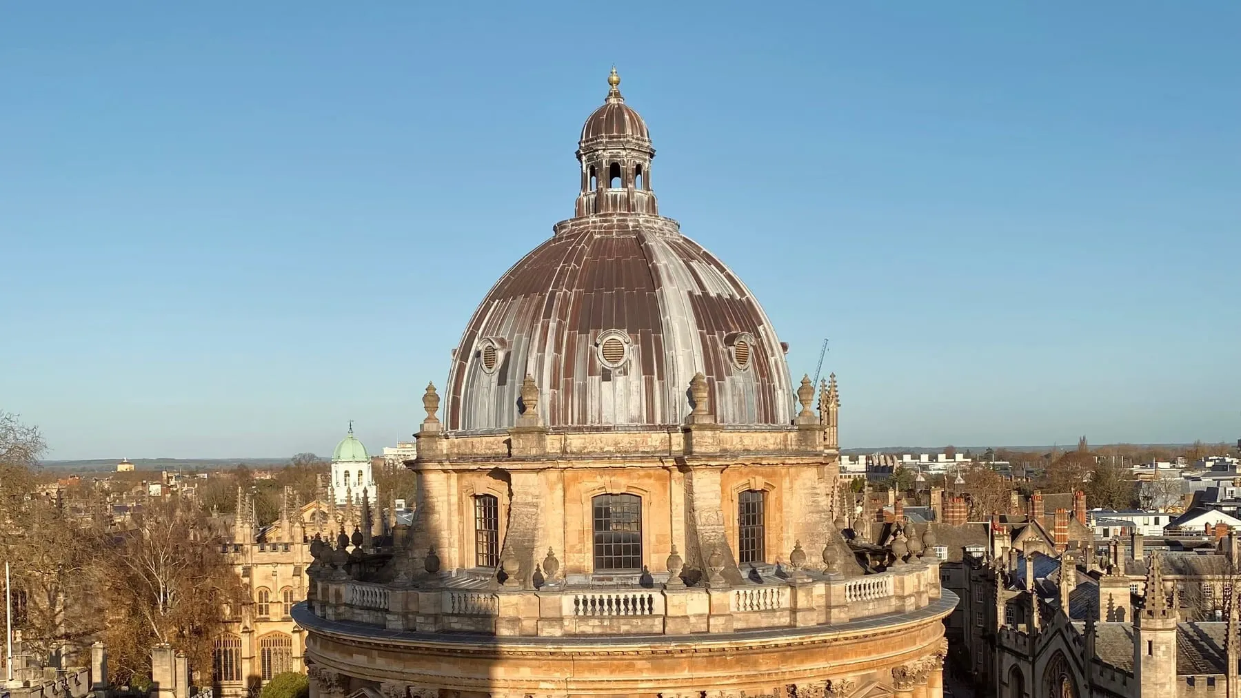 The dome of the Radcliffe Camera in Oxford lit by low sun, with college roofs and the city behind