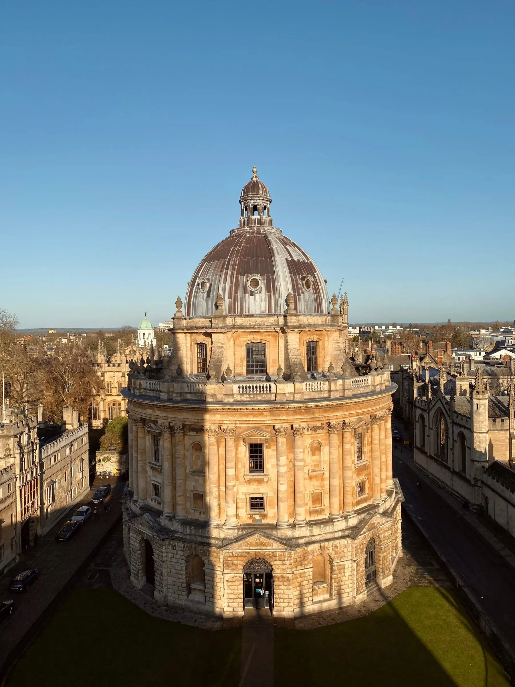The domed Radcliffe Camera in Oxford, honey-coloured stone lit by low sun with college roofs behind