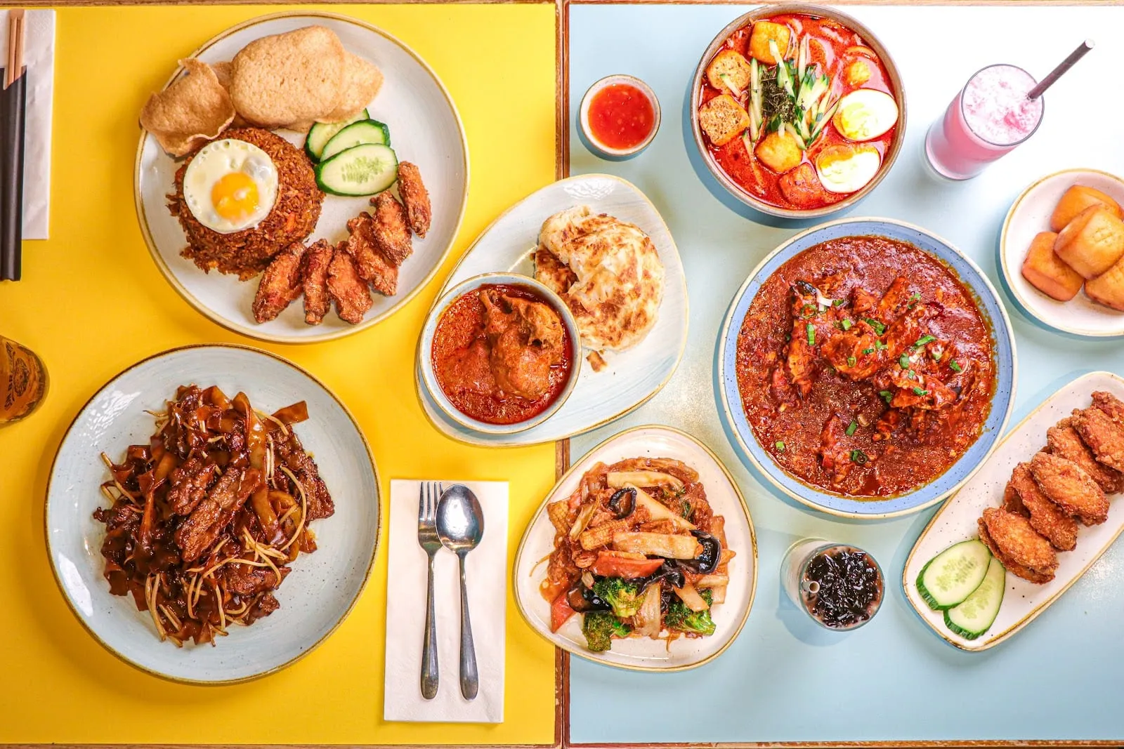 An overhead shot of a table with nasi lemak, fried egg, prawn crackers and cucumber on one side, and Singapore chilli crab with mantou buns on the other