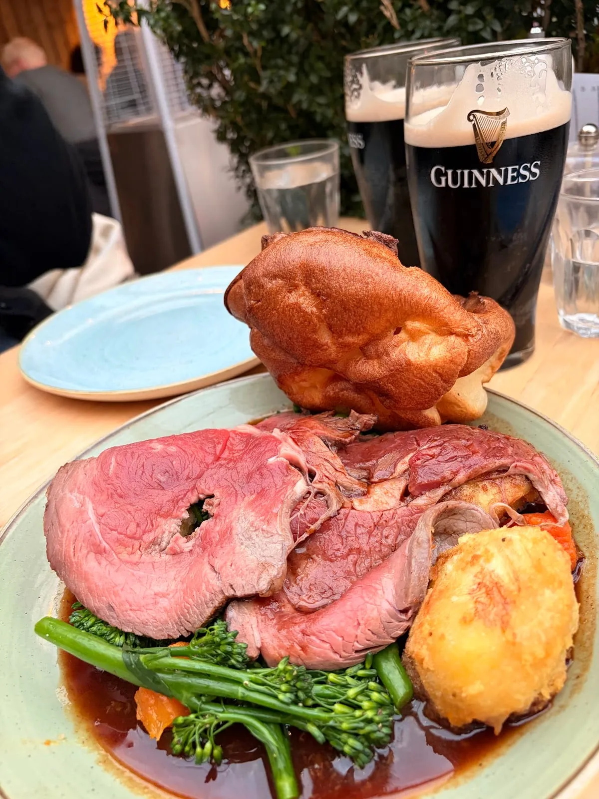 Two pints of Guinness on a table in the garden of The Red Lion and Sun, beside a Sunday roast with a tall Yorkshire pudding