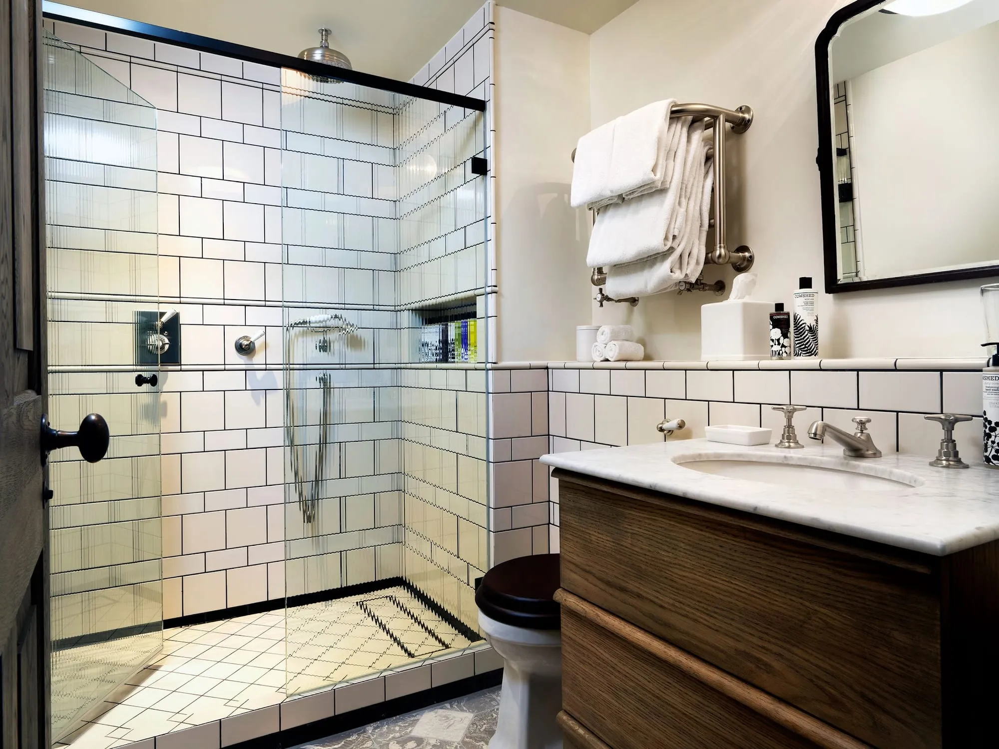 A bathroom at Redchurch Townhouse with white subway tile, a walk-in shower and Cowshed products on the marble-topped vanity