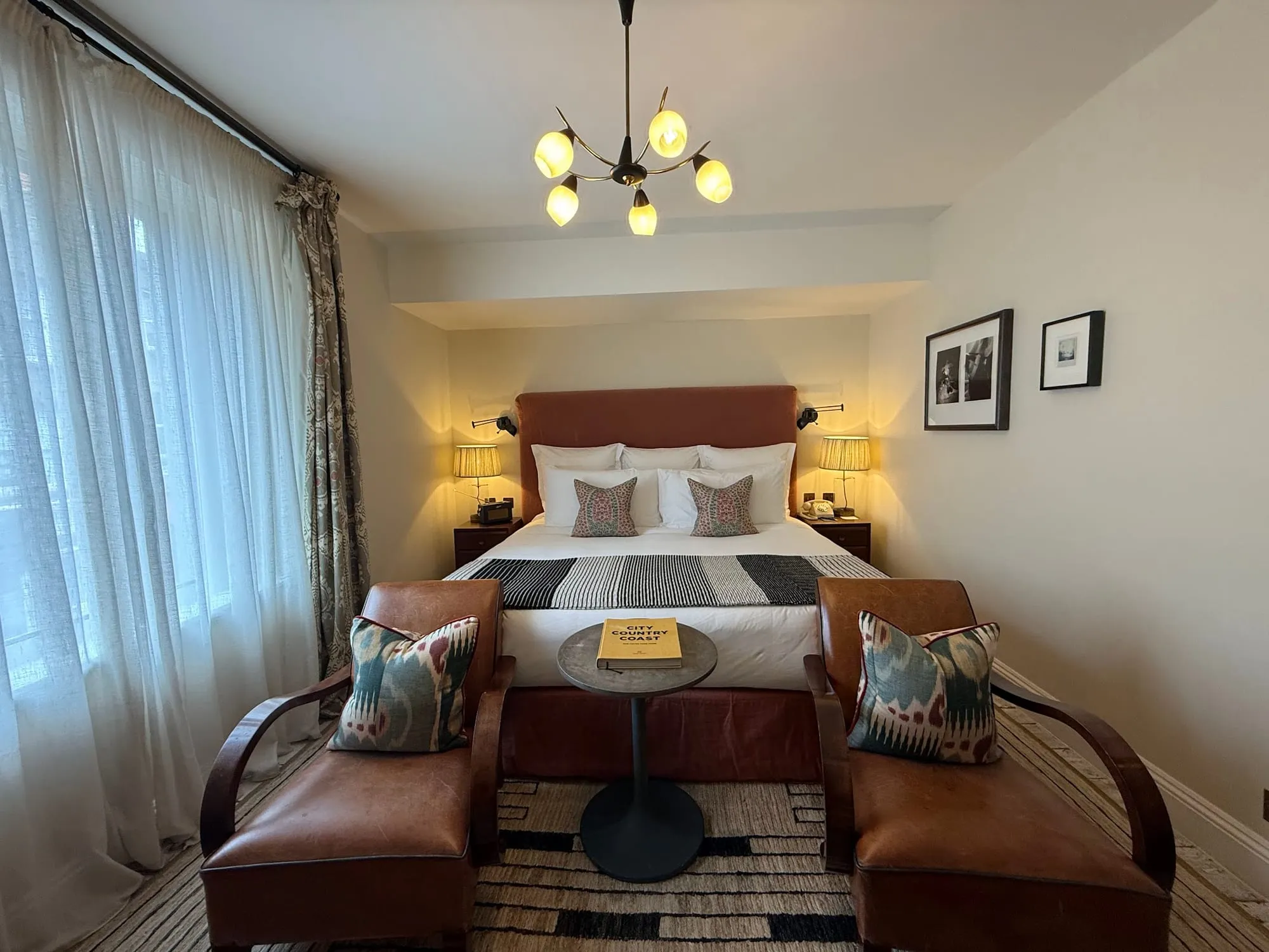 A room at Redchurch Townhouse with a rust velvet headboard, a six-arm chandelier and two leather armchairs