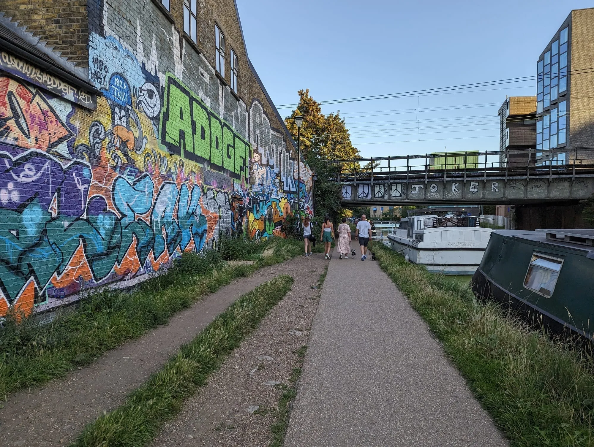 The Regent's Canal towpath in east London, with a long graffiti-covered wall on one side and moored narrowboats on the other