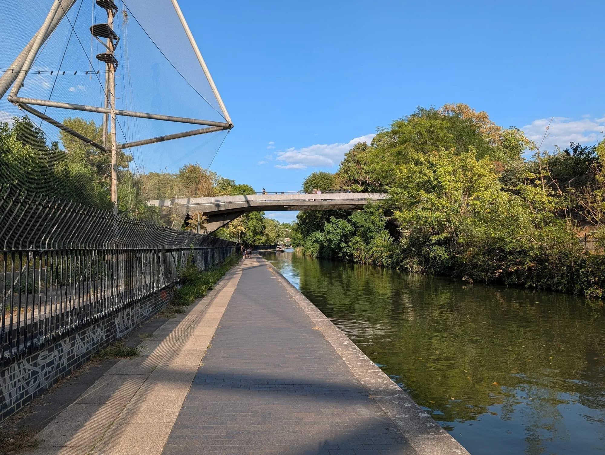 The Regent's Canal towpath running toward Snowdon Aviary at London Zoo, its metal frame visible over the water