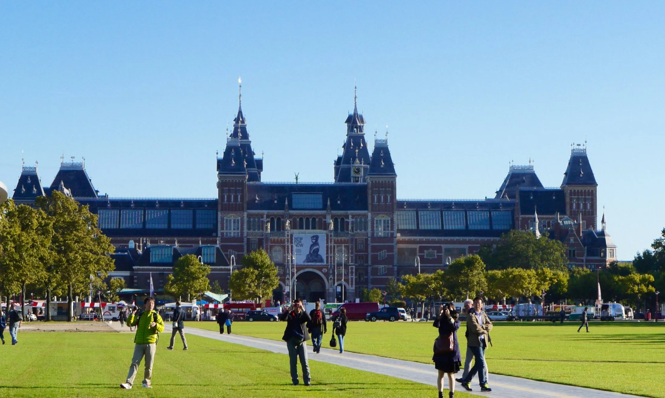 The Rijksmuseum's twin-towered main building seen across the lawns of Museumplein, with visitors walking the paths in front of it