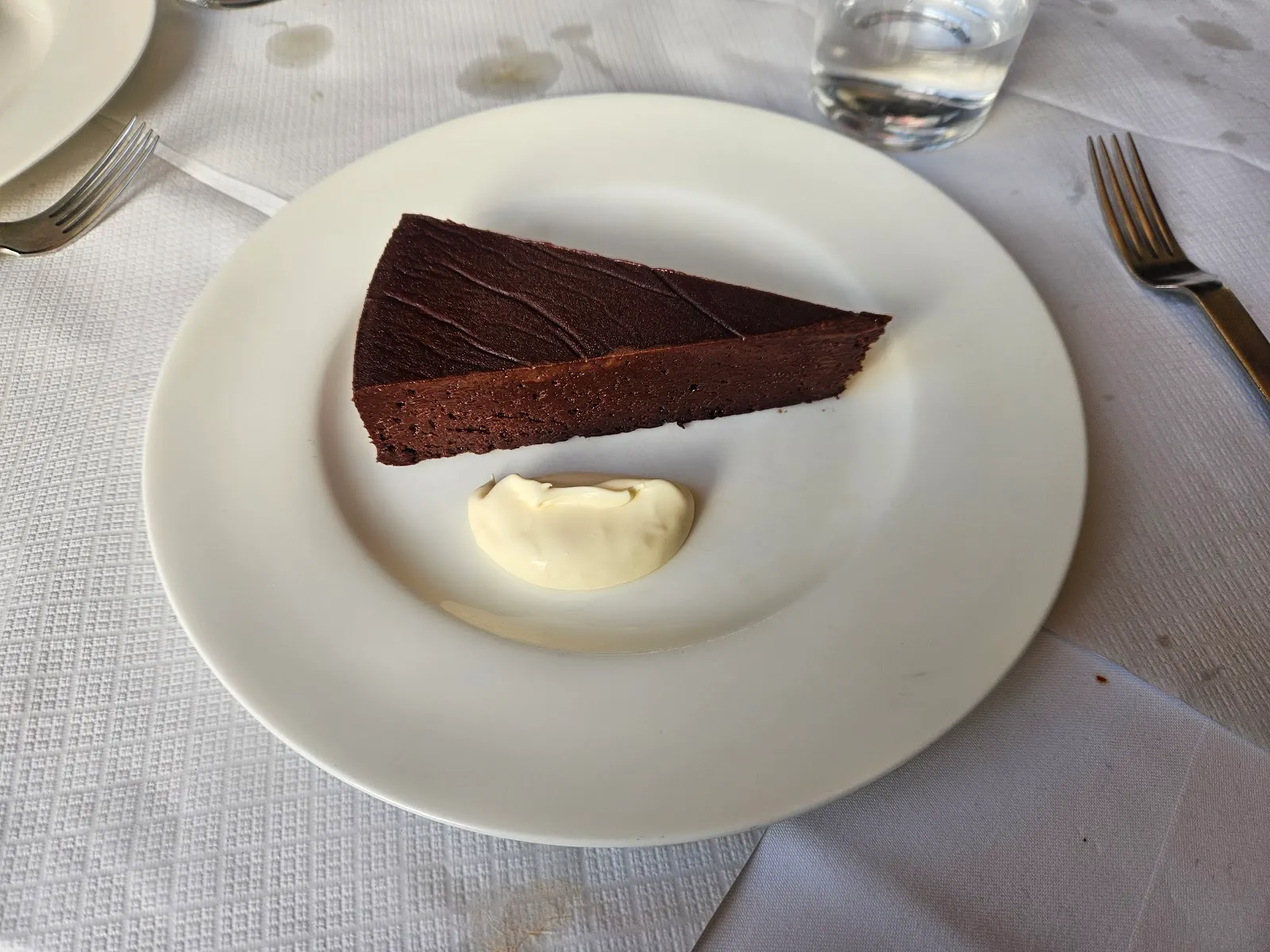 A triangular slice of dark chocolate nemesis cake with a spoon of crème fraîche, on a white plate