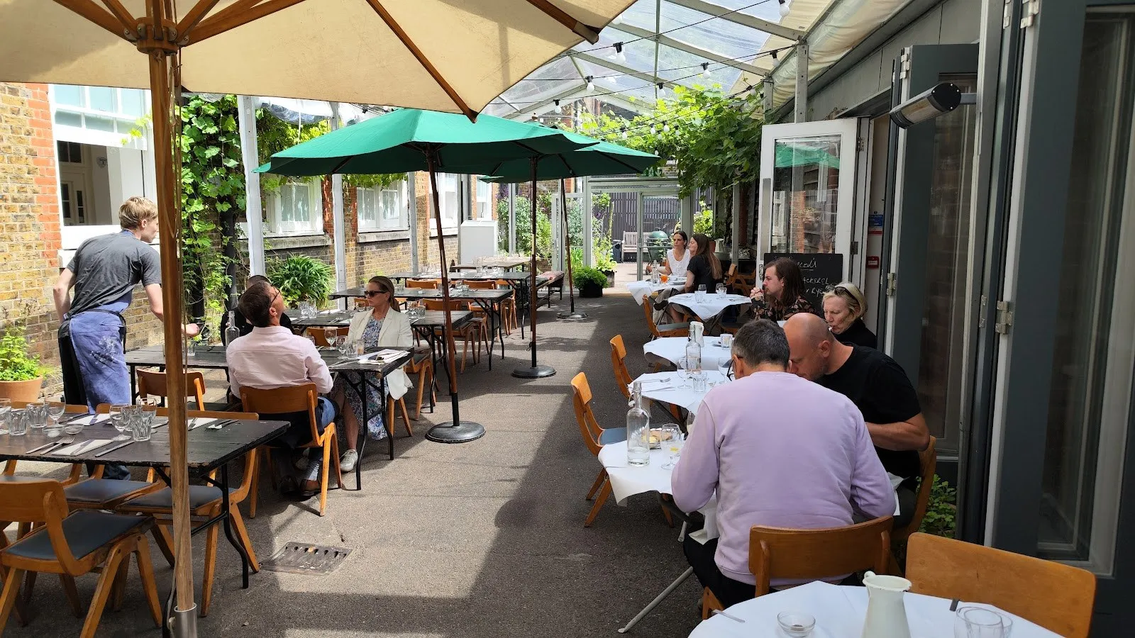 Diners at tables under umbrellas on the covered terrace at Rochelle Canteen