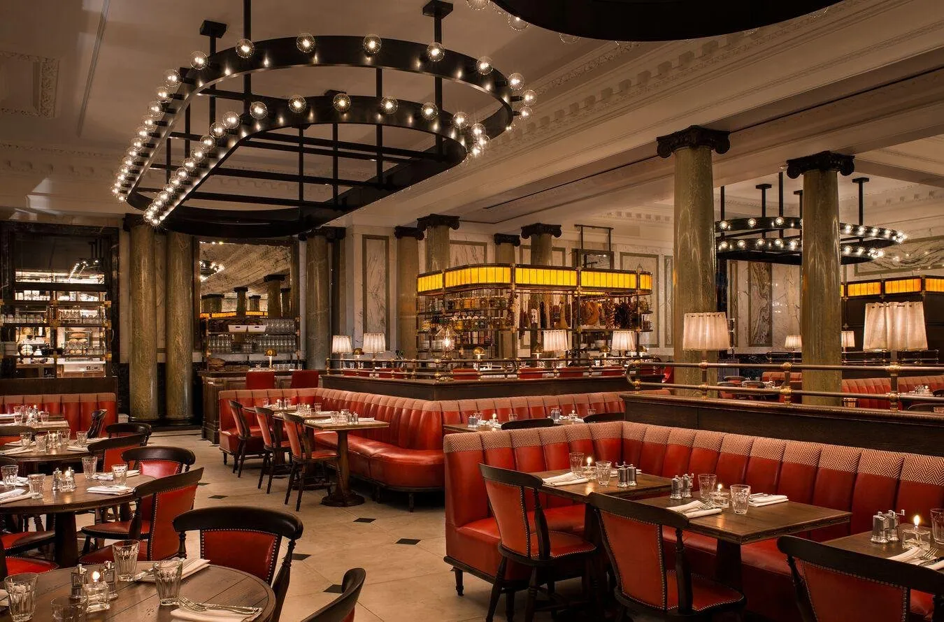 The bar and restaurant at Rosewood London, with red leather booths, marble columns and a ring-shaped chandelier
