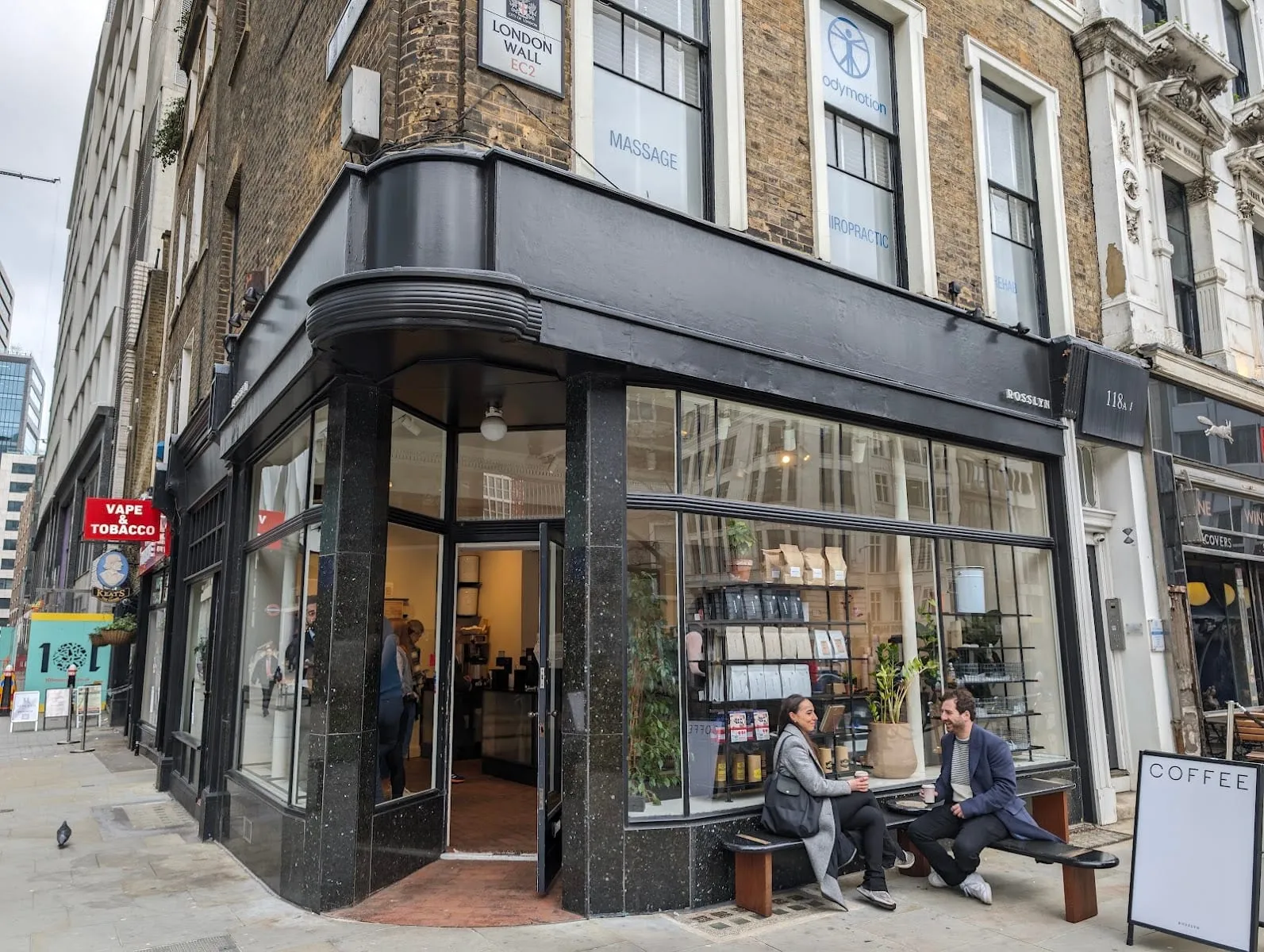 The corner shopfront of Rosslyn Coffee on London Wall, with two customers on the outside bench holding takeaway cups