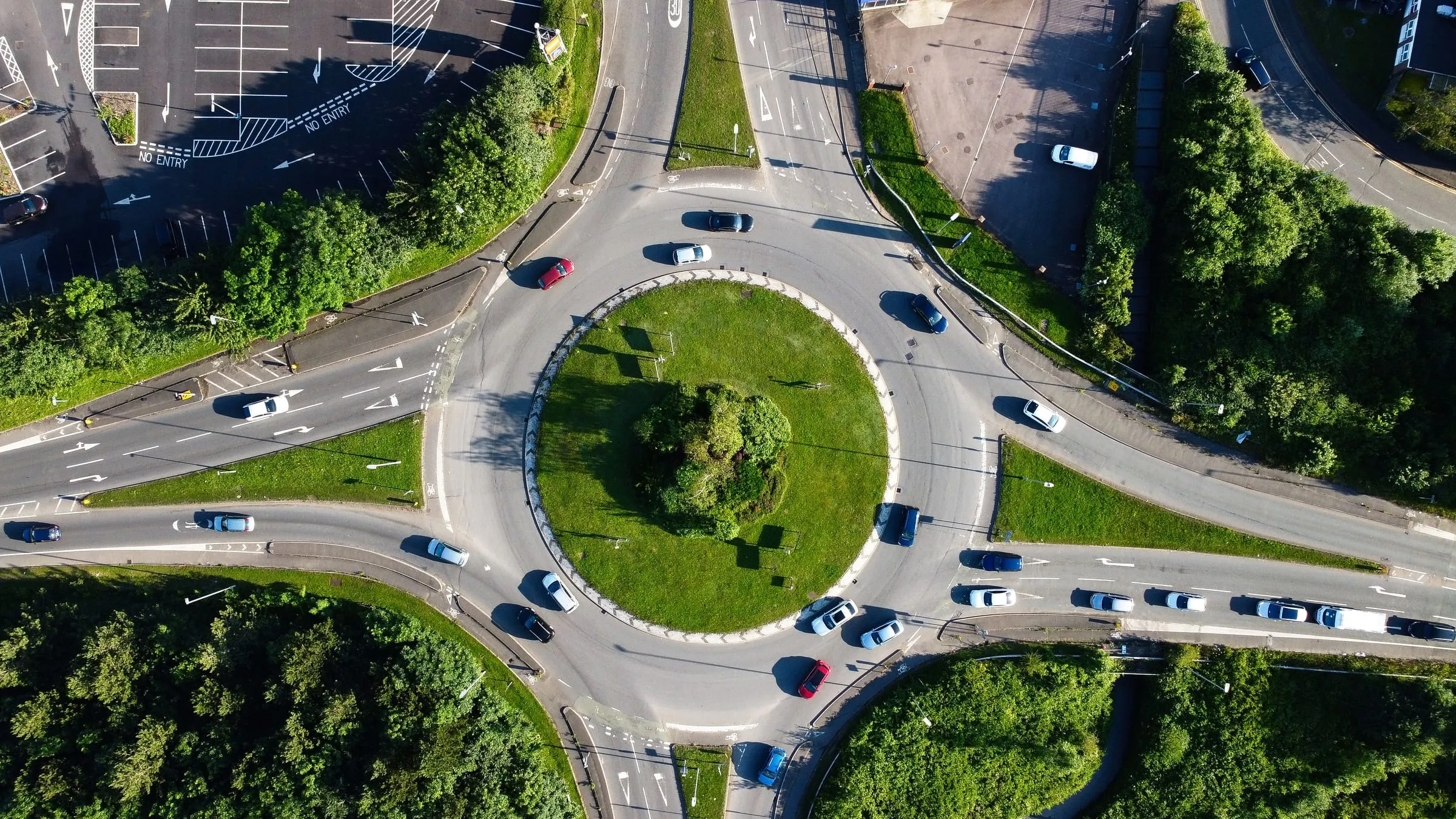 A British roundabout seen from directly above, cars circling a grass island with four roads feeding into it