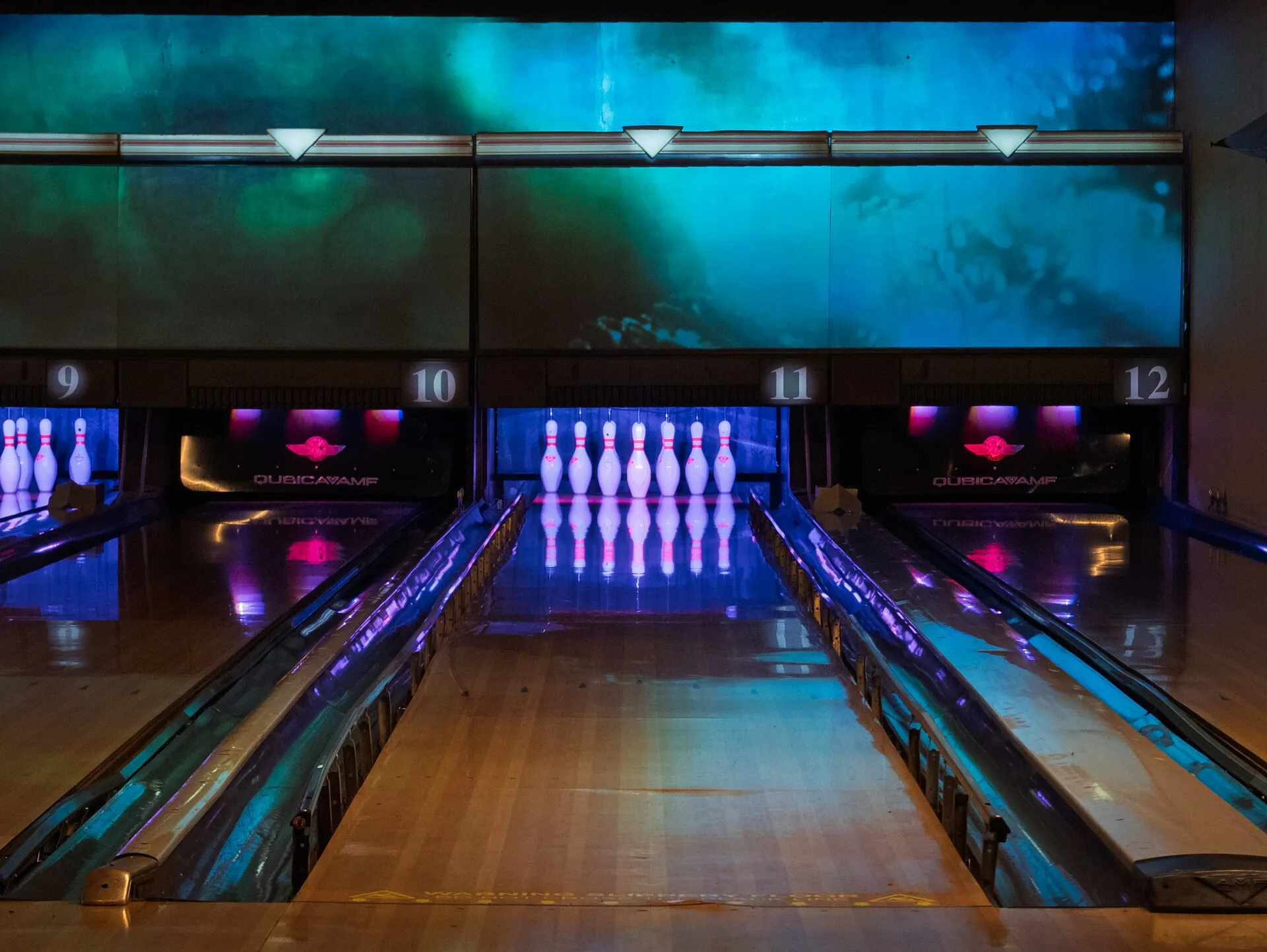 Rowans' bowling lanes 9 to 12 lit in blue and purple, with pins glowing under ultraviolet light and a projected cloudscape above