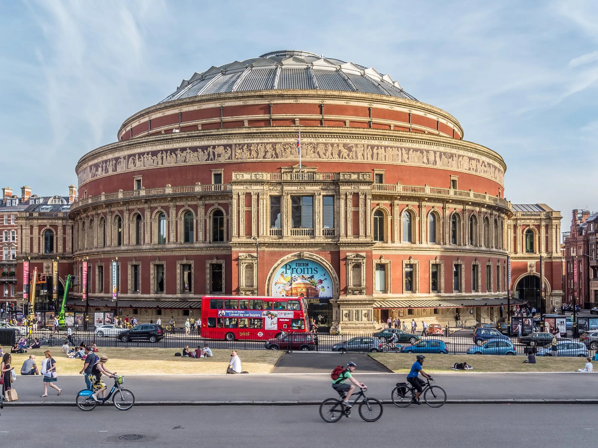 The red-brick Royal Albert Hall with a BBC Proms banner across its entrance arch and a red London bus passing in front