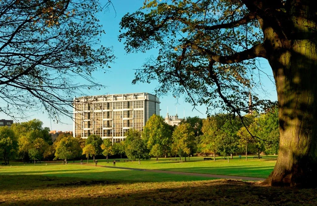 The Royal Garden Hotel building seen across a grassy lawn with mature trees in Kensington Gardens