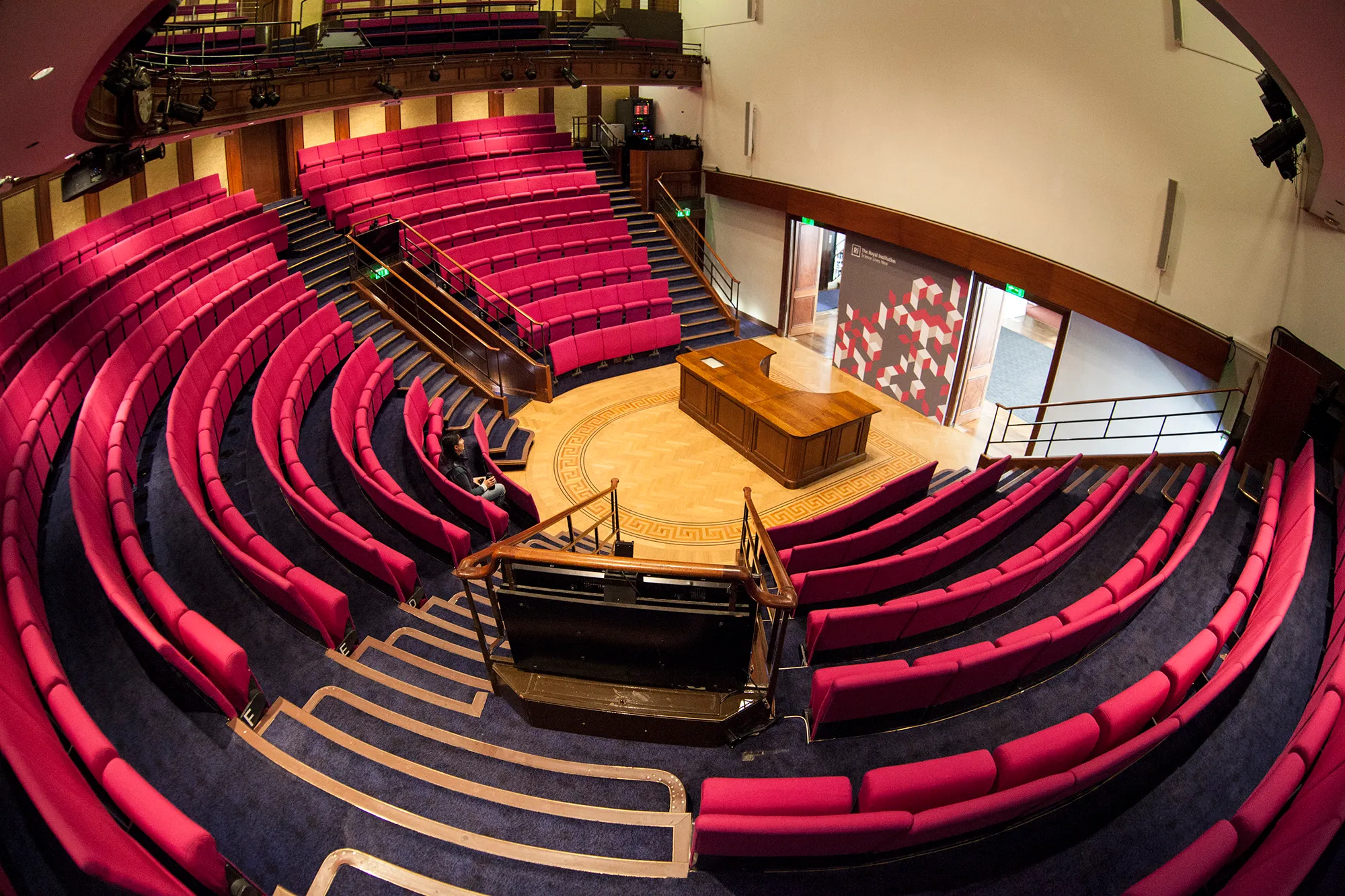 The Royal Institution's lecture theatre, tiers of red seats curving in a semicircle around a wooden demonstration bench on the floor below