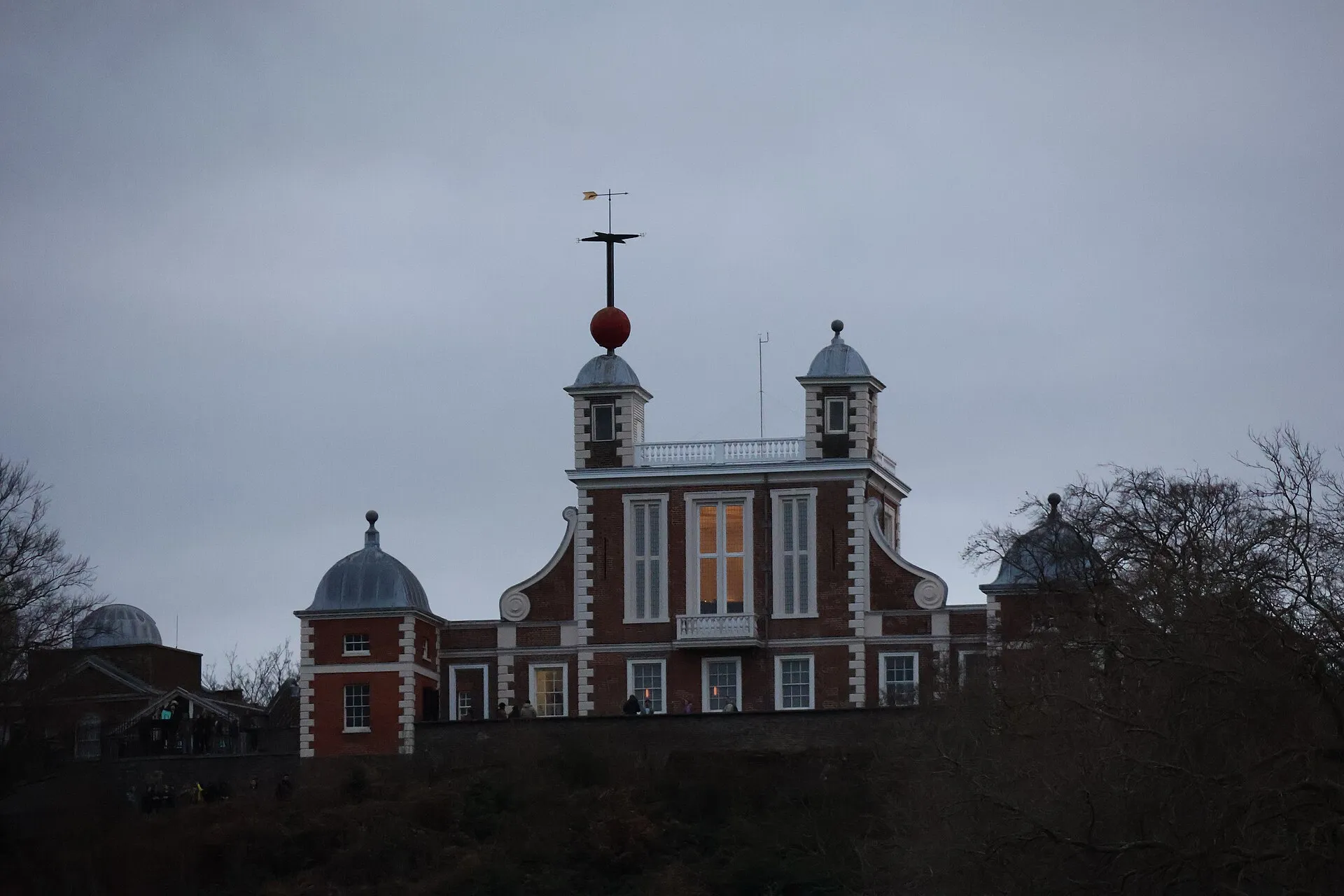 Flamsteed House at the Royal Observatory Greenwich at dusk, the red time ball raised on its mast above the turret and the Octagon Room windows lit from inside