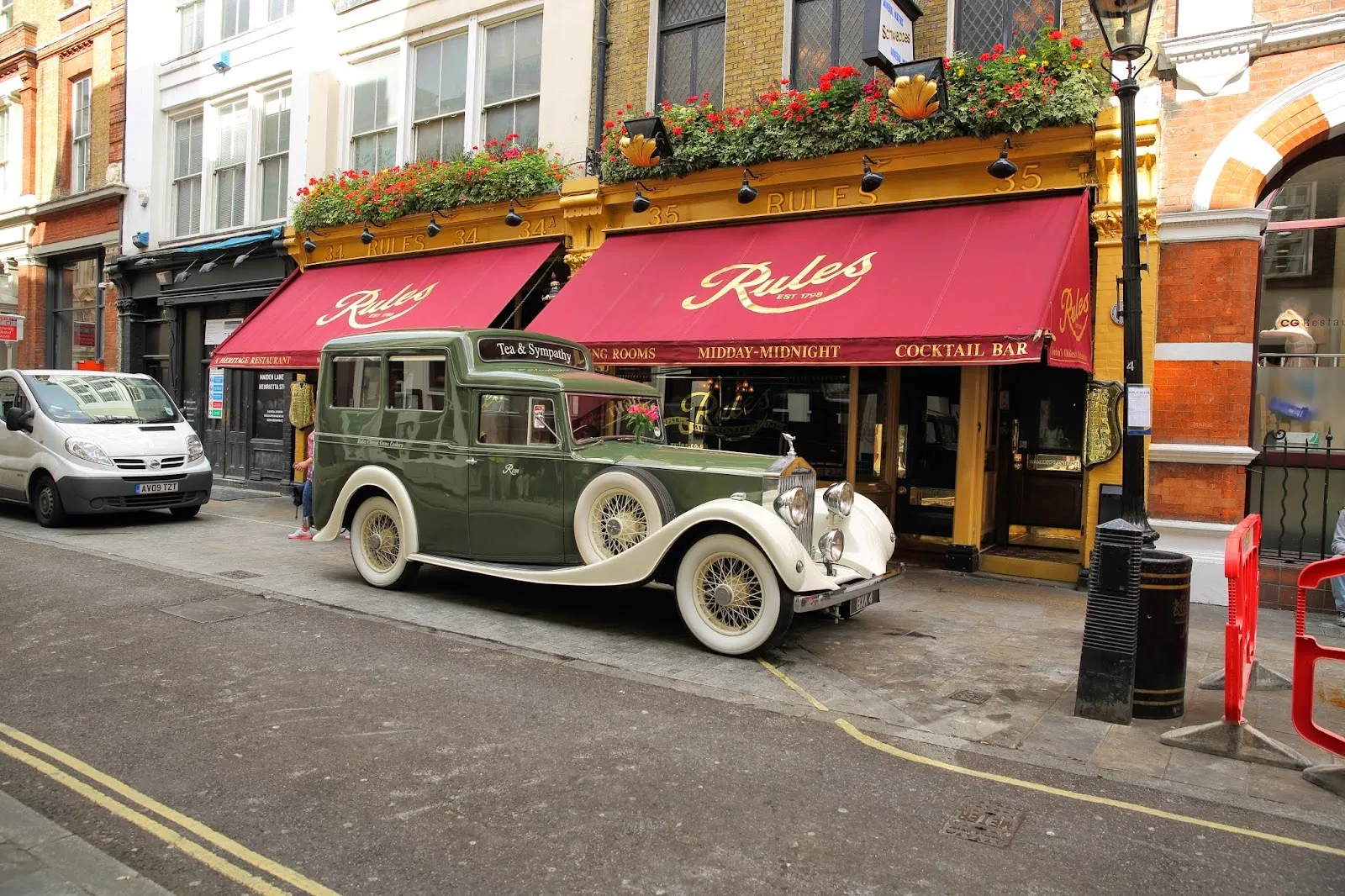 A vintage green Rolls-Royce parked outside Rules restaurant in Covent Garden, beneath red awnings reading Rules, Est 1798