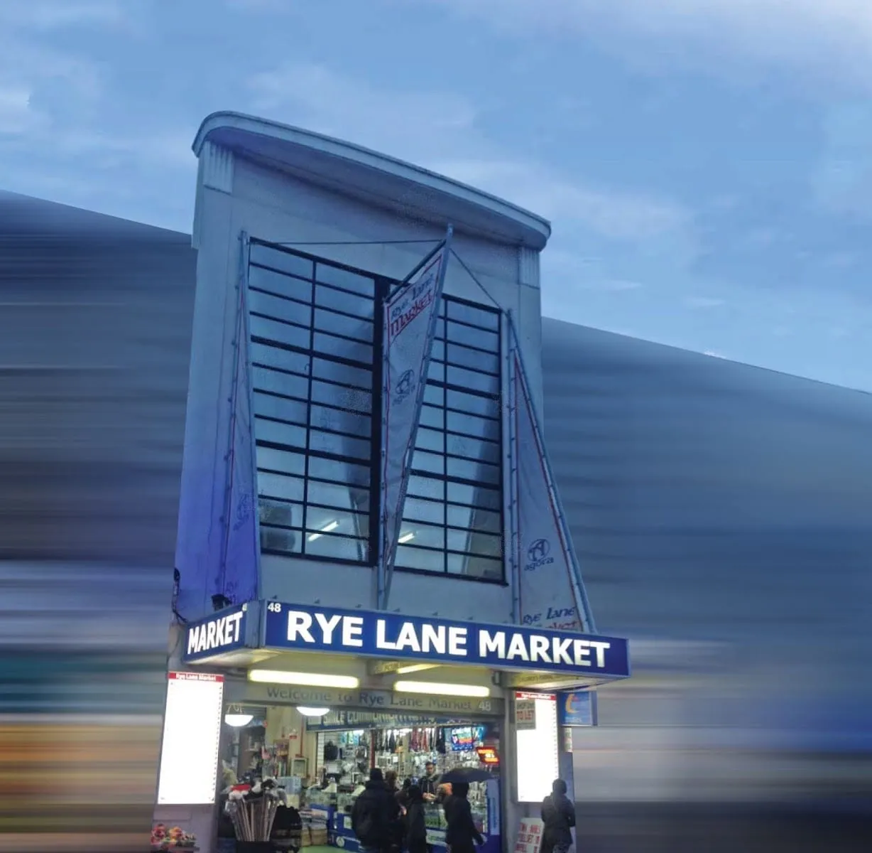 The tall blue frontage of Rye Lane Market at number 48, lit up at dusk
