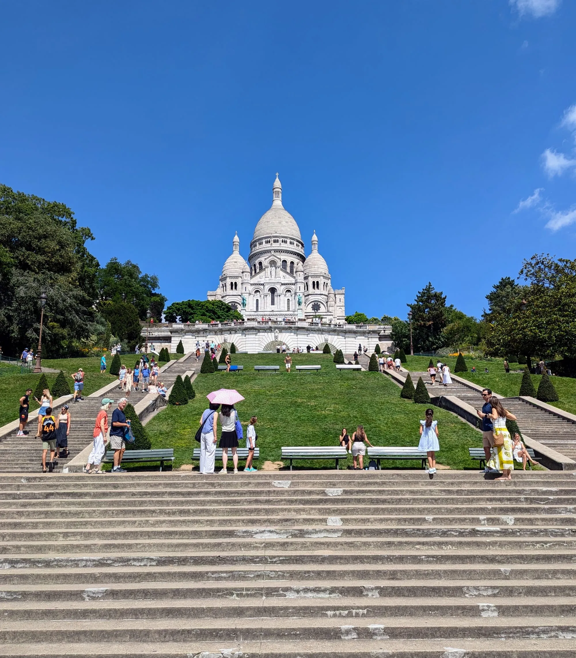 The white domes of the Sacré-Cœur at the top of Montmartre, above lawns and long flights of steps busy with visitors