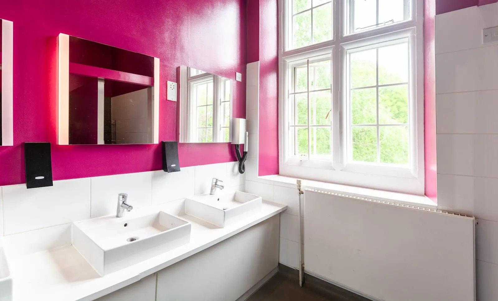 The attached bathroom at Safestay London Kensington Holland Park, with twin sinks, illuminated mirrors and a large sash window