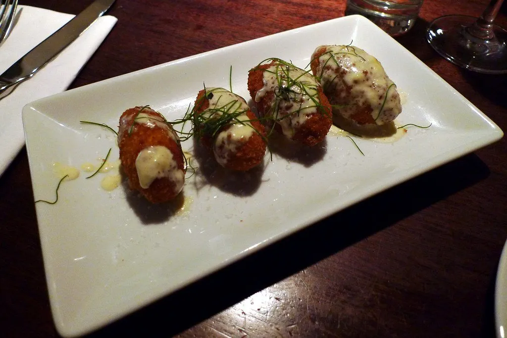 Croquetas topped with sauce on a white plate