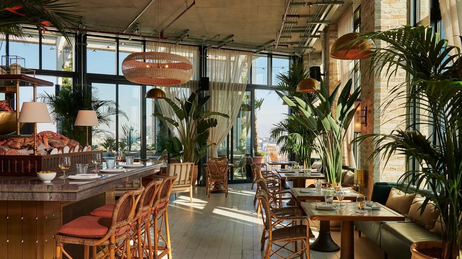 Seabird's indoor dining room, with a marble-topped bar carrying a raised display of crab, prawns and shellfish on ice, rattan bar stools and armchairs, tall palms, and glazed doors onto the terrace
