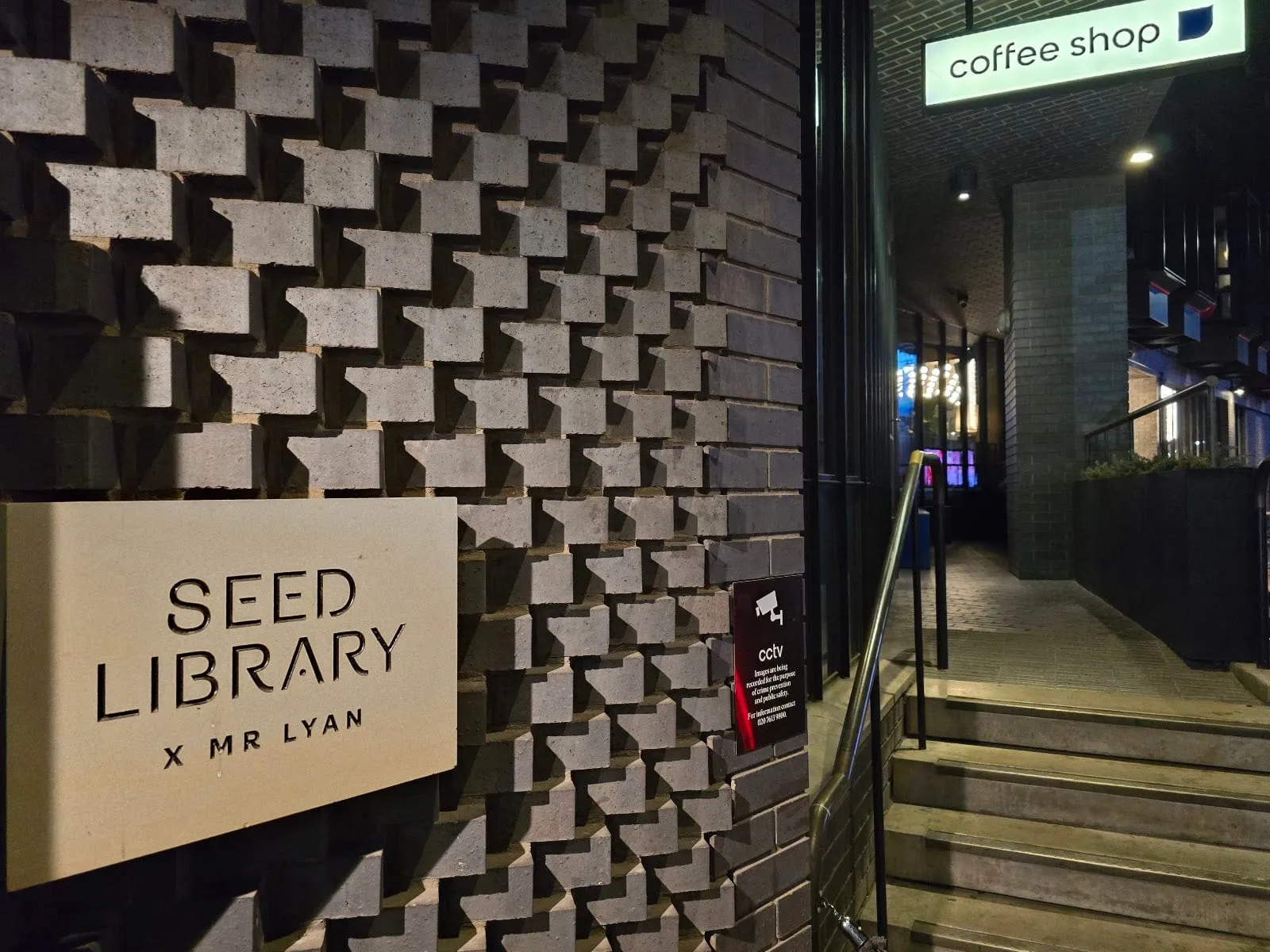 A Seed Library x Mr Lyan sign on a patterned brick wall, beside steps up to a coffee shop entrance