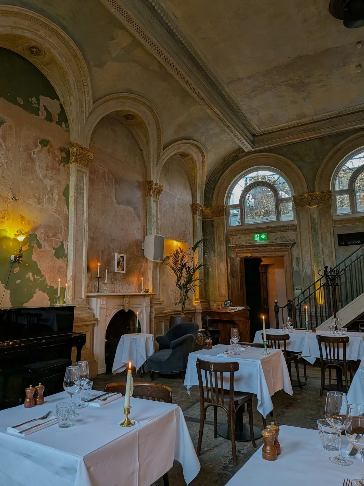 The dining room at Sessions Arts Club, tall arched windows and walls of peeling green and pink plaster above candlelit tables with white cloths