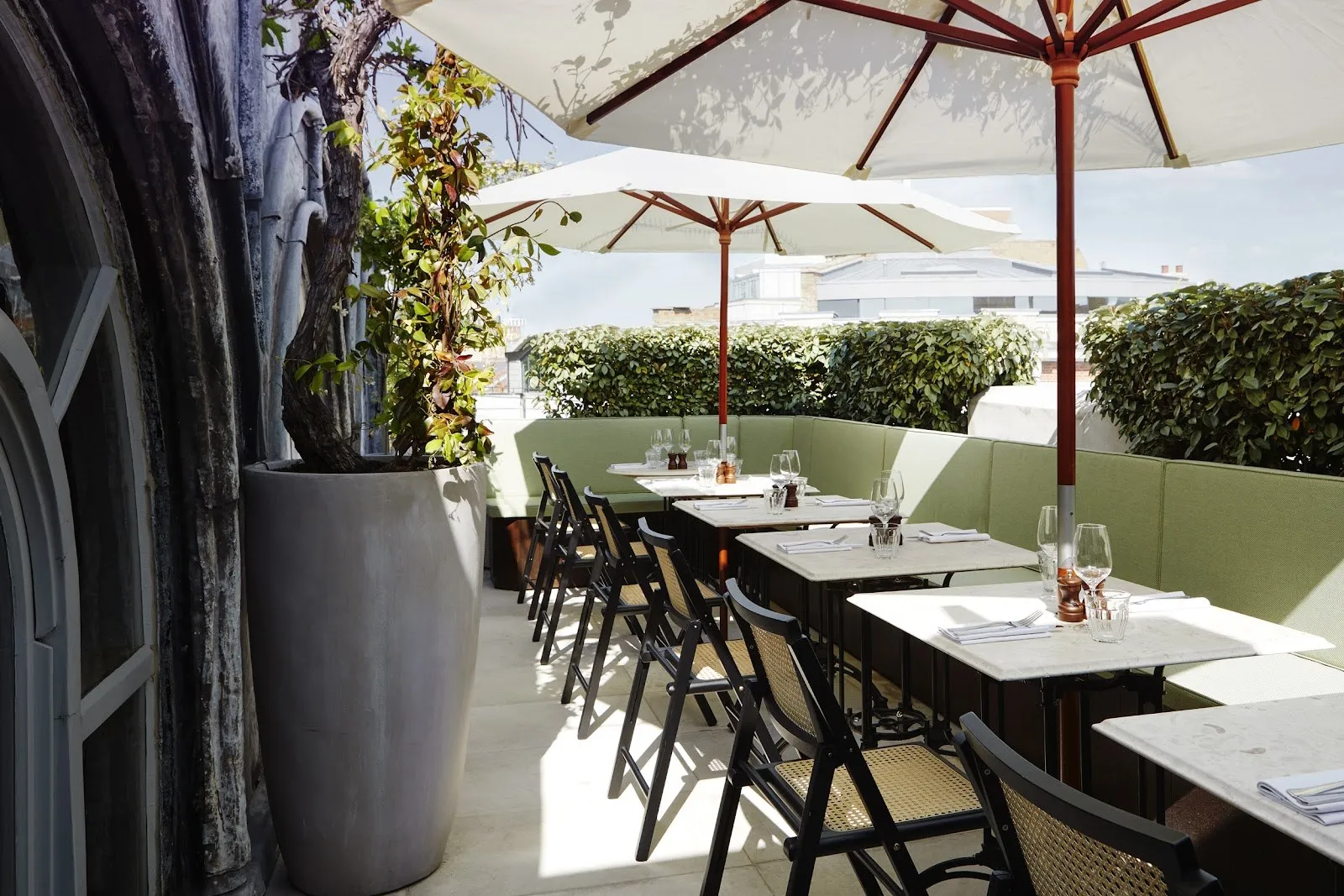 Tables under white umbrellas on a terrace beside an arched window