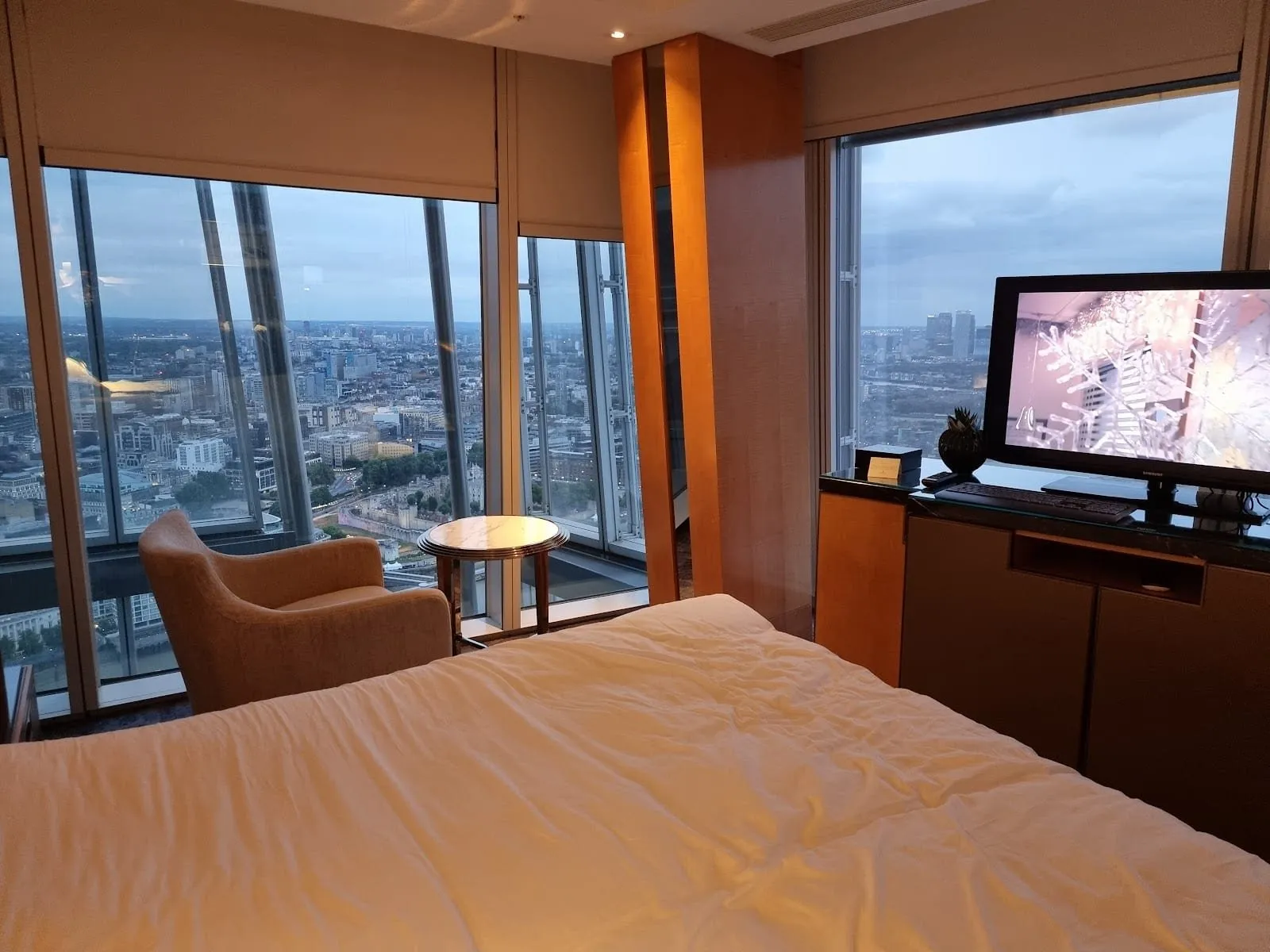 A corner room high in Shangri-La The Shard with floor-to-ceiling windows looking down on the Tower of London and east along the river to Canary Wharf, a beige armchair and marble side table by the glass