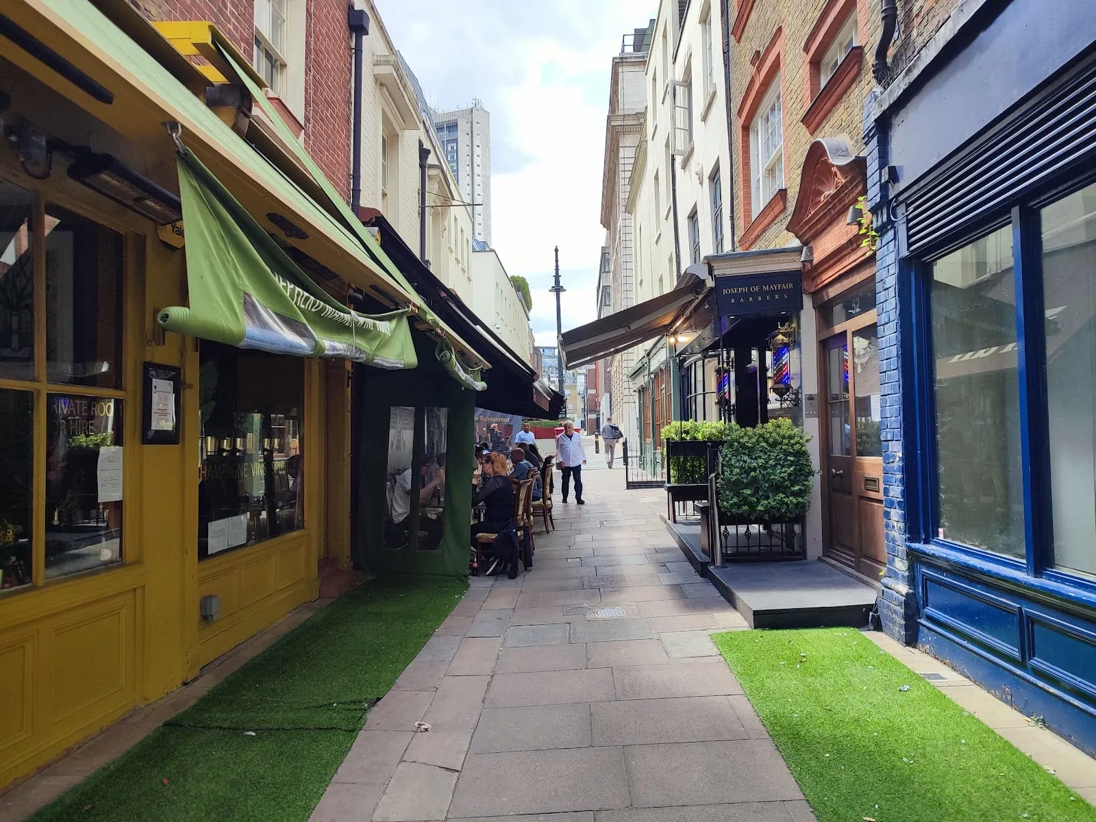 A narrow pedestrian lane in Shepherd Market lined with independent shopfronts, including a barber and a restaurant