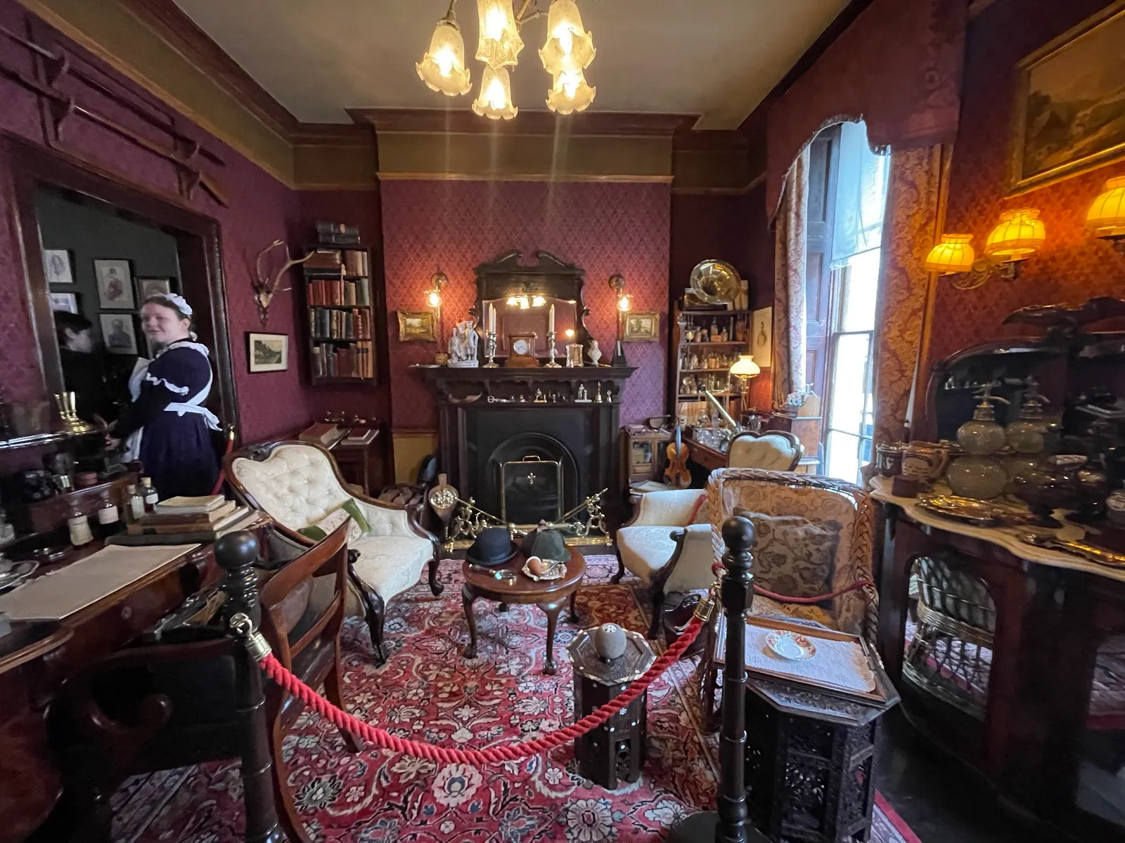 The recreated sitting room at the Sherlock Holmes Museum, with a guide in Victorian dress beside the fireplace and armchairs roped off for viewing