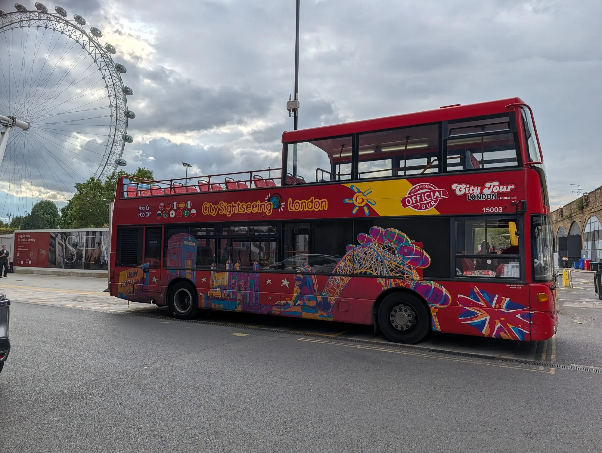 A red open-top City Sightseeing tour bus in London, its upper deck open to the sky
