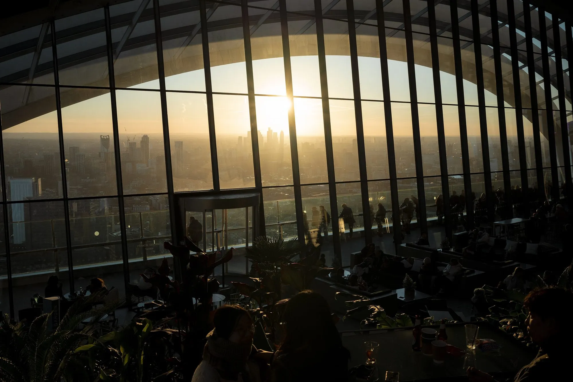 Low winter sun shining through the curved glass wall of the Sky Garden, with visitors in silhouette at the tables