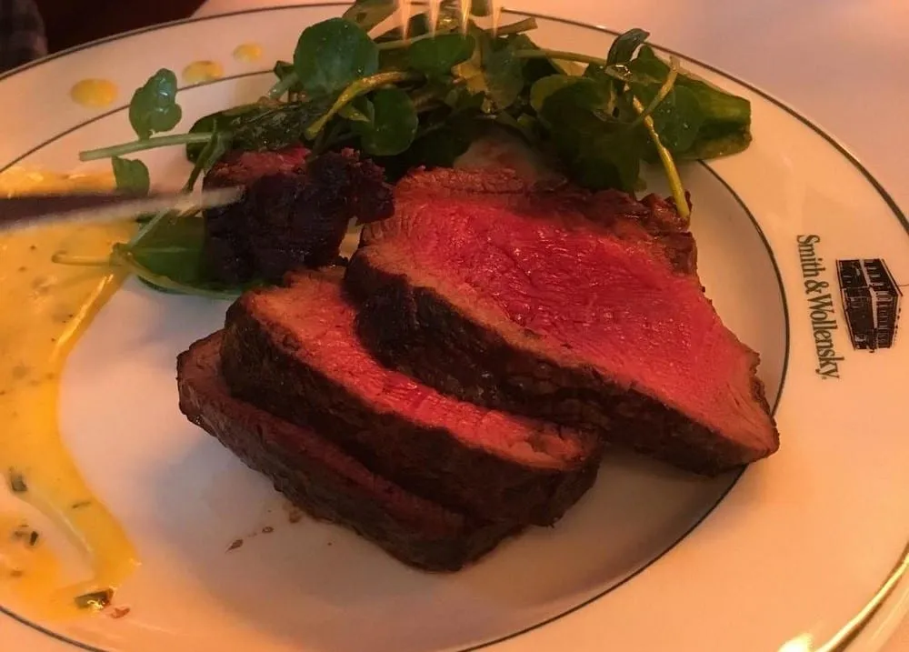 Slices of rare steak with watercress and a smear of béarnaise, on a white plate printed with the Smith & Wollensky crest on the rim