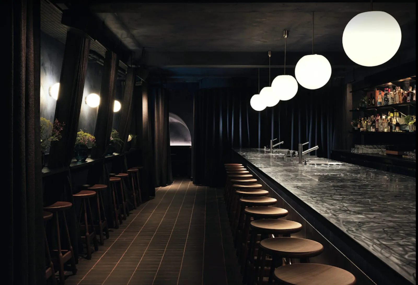 SOMA Soho's long stainless steel counter with wooden stools, globe pendant lights and dark curtained walls