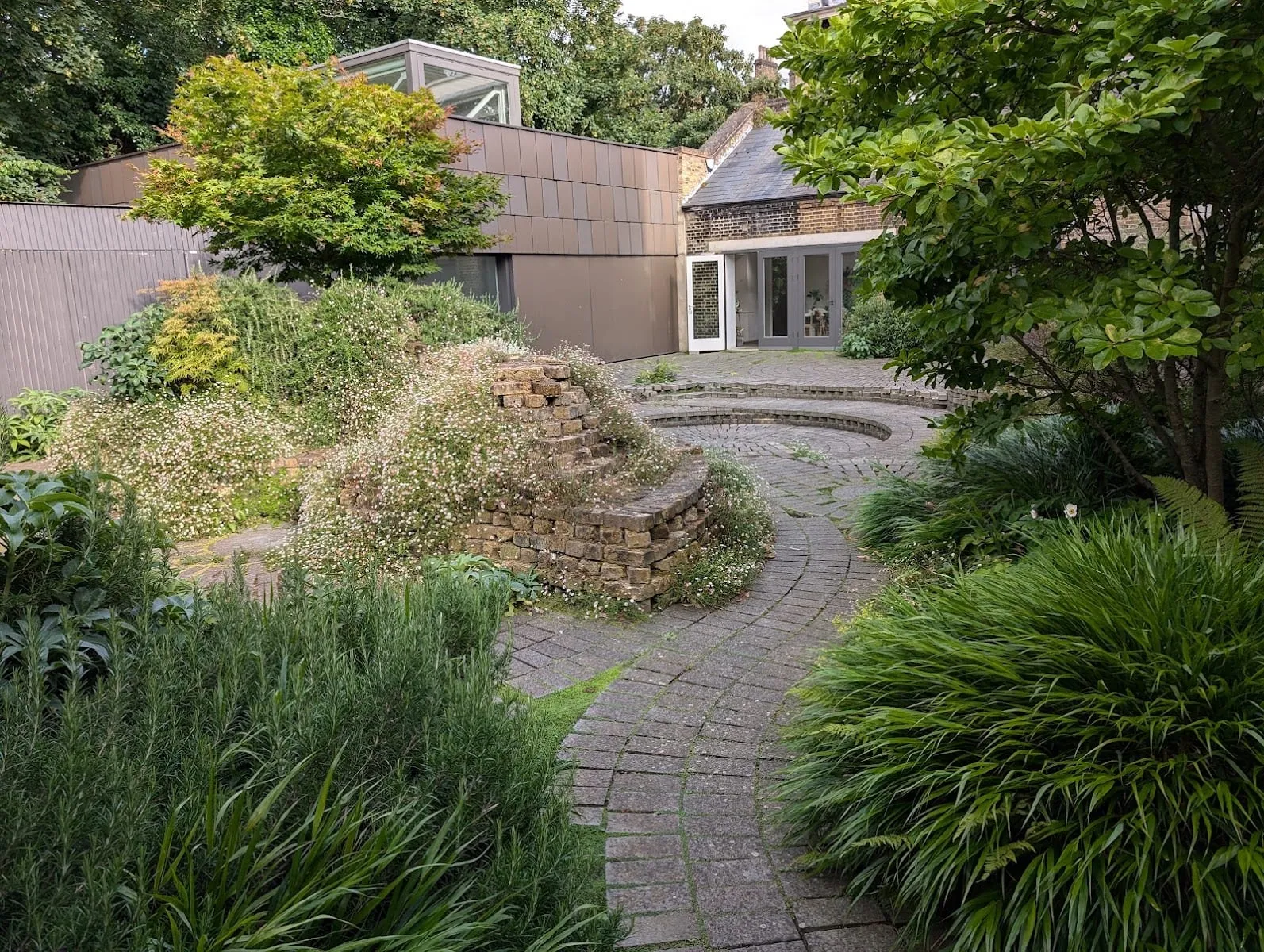 A quiet paved garden behind the South London Gallery, with a curved brick wall, wildflowers and a modern extension building