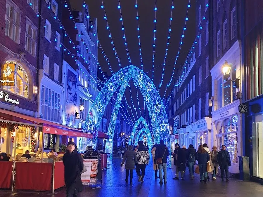 Arches of blue light studded with stars over South Molton Street at night, with Caffè Concerto's terrace on the left and shoppers walking under them