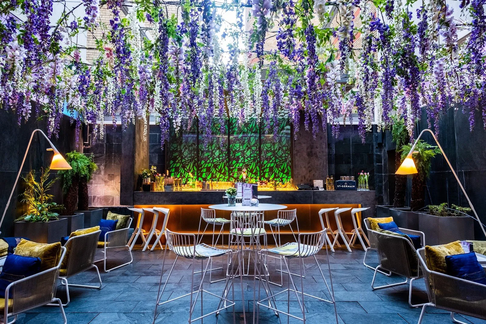 The wisteria-hung courtyard bar at South Place Hotel, with a stone bar counter, hanging lanterns and outdoor seating under strings of hanging flowers