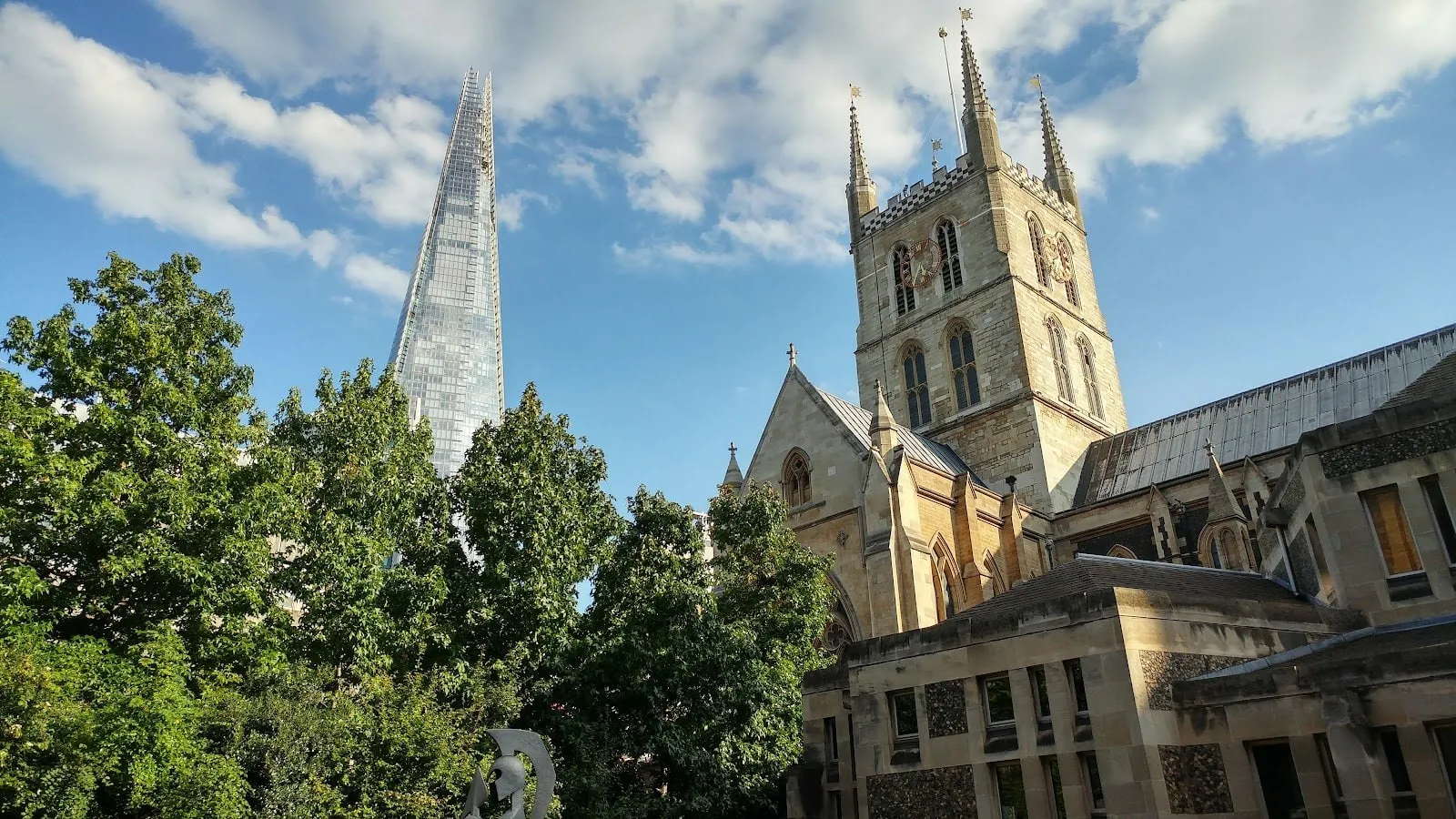 The pinnacled stone tower of Southwark Cathedral and its roof, with the glass spire of the Shard rising above the trees to the left